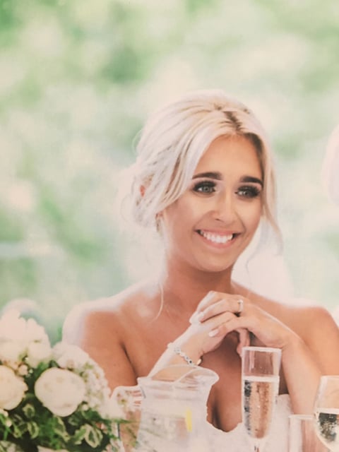 Woman with platinum blonde hair smiling at wedding reception with white flowers and champagne glass