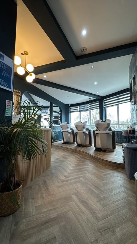 Modern spa or salon waiting area with herringbone wood flooring, cream armchairs, blue walls, geometric ceiling design, and decorative plants